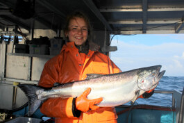 Eva präsentiert einen frisch gefangenen Lachs an Board der Suki, im Hintergrund der Ozean